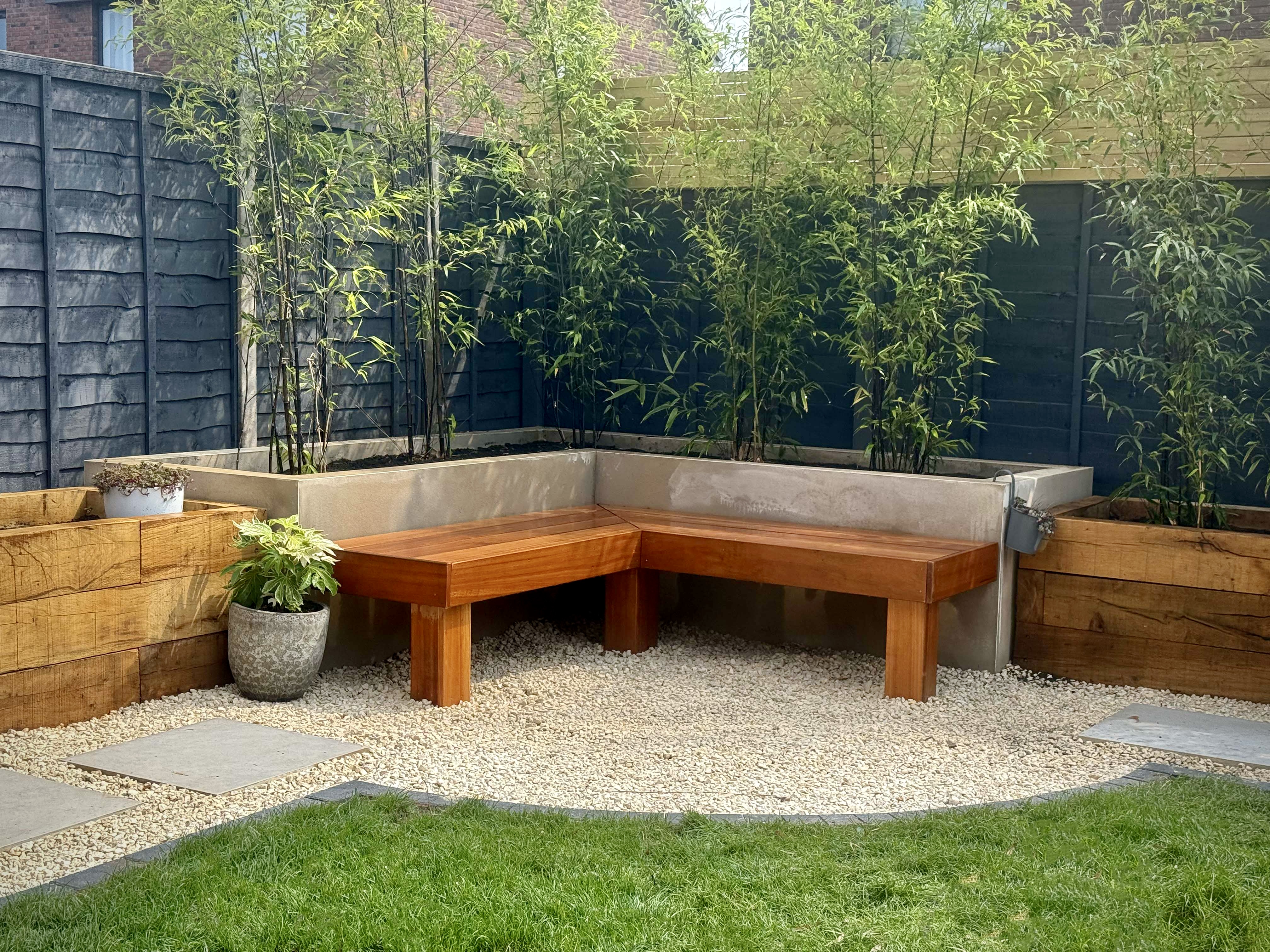 The finished Hassocks garden built to match the visualisation — a bespoke hardwood corner bench set within raised rendered planters and bamboo screening, by Brunswick Landscapes